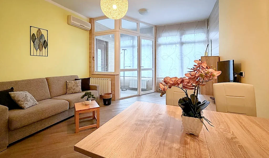 Svetel dnevni prostor apartmaja Isonzo v Bovcu z jedilno mizo, kavčem in lastno kuhinjo.