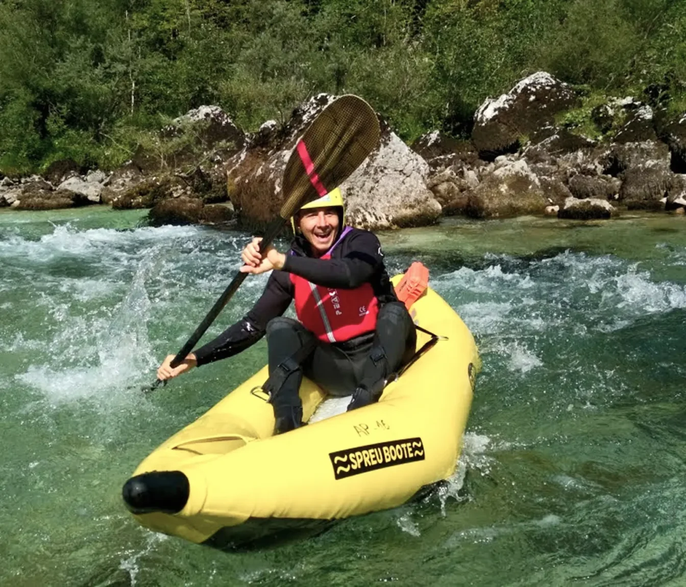 Nasmejan gost z veslom nad glavo na rumenem guppy čolnu na Soči pri Bovcu.