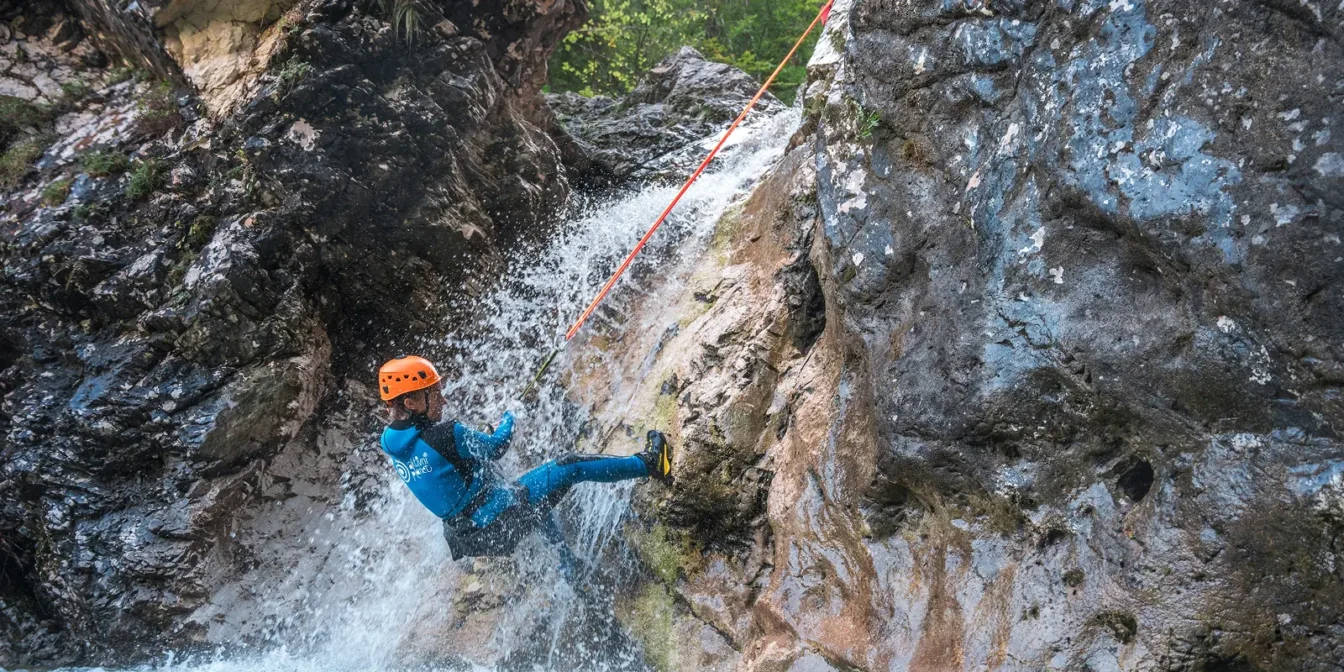 Kanjonist se spušča po vrvi ob skalni steni skozi slap v soteski Fratarica, Loška stena.