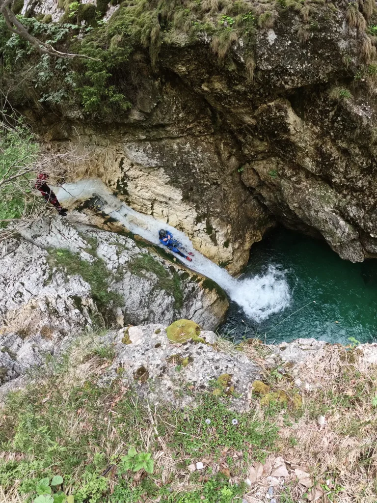 Pogled z višine na spust po naravnem toboganu v smaragdni tolmun v kanjonu Rio Ronc v dolini Rezije v Italiji.
