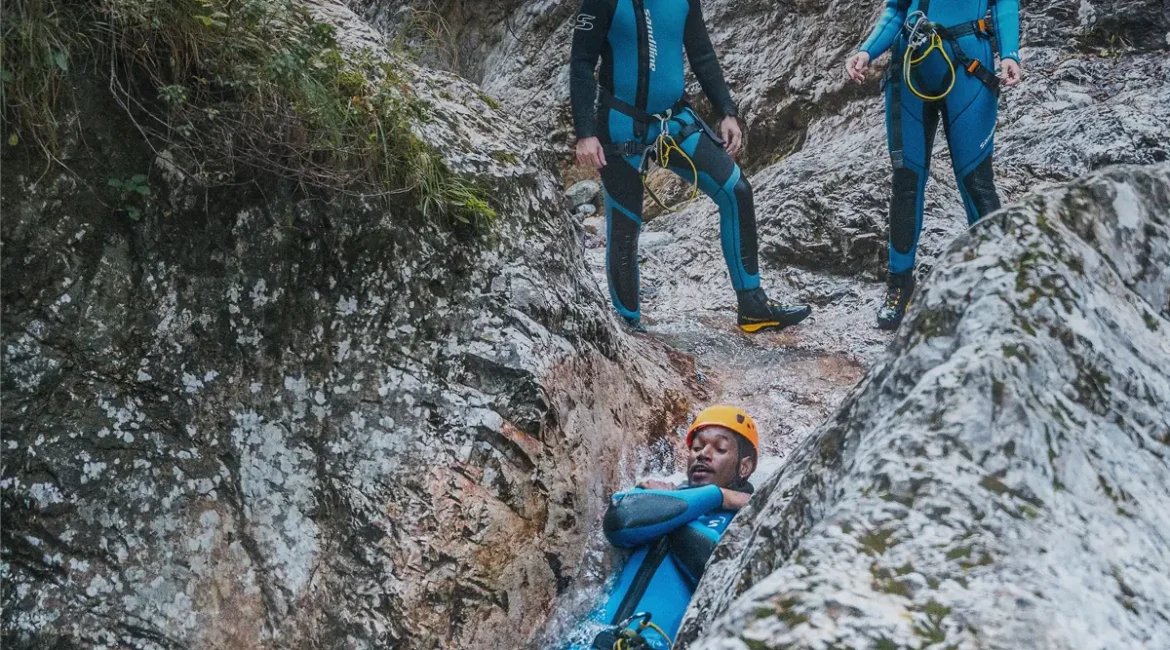 Skupina v neoprenu se po naravnem toboganu spušča v tolmun v soteski Sušec pri Srpenici, kanjoning z Aktivni Planet pri Bovcu.