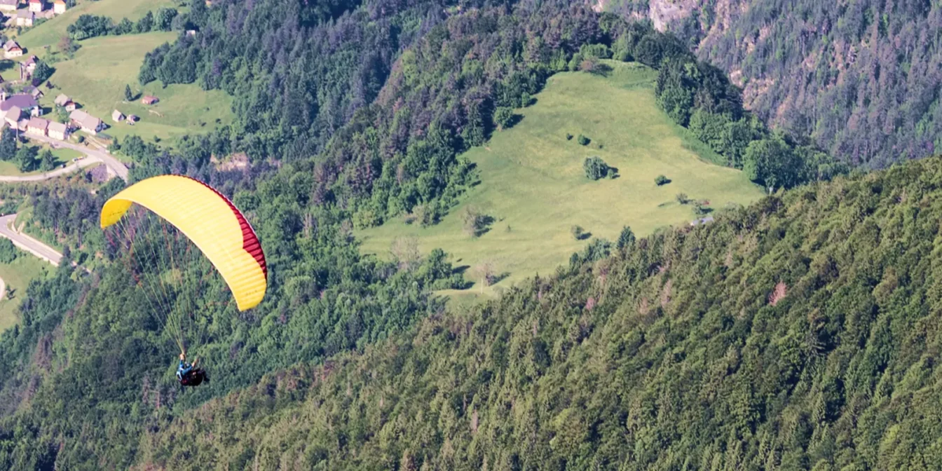 Jadralno padalo nad zelenimi pobočji in vasjo v dolini Soče pri Bovcu