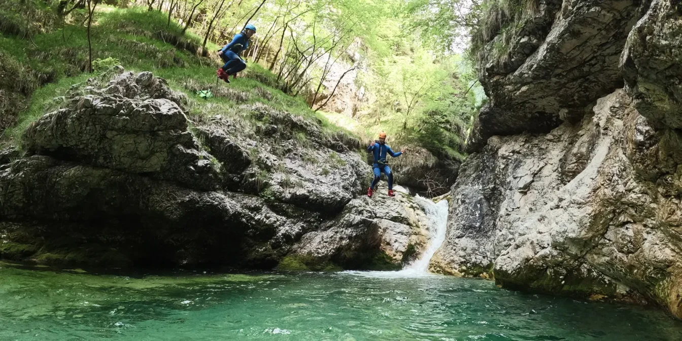 Udeleženec sredi skoka v smaragdni tolmun ob manjšem slapu v kanjonu Rio Ronc v dolini Rezije.
