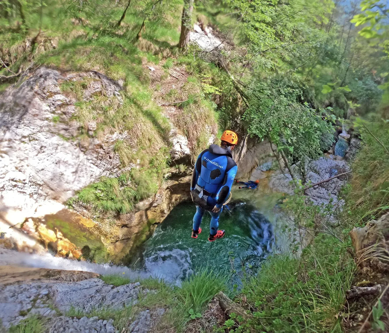 Udeleženec pred skokom v zelen tolmun ob slapu, gozdnata soteska v dolini Rezije v Italiji.