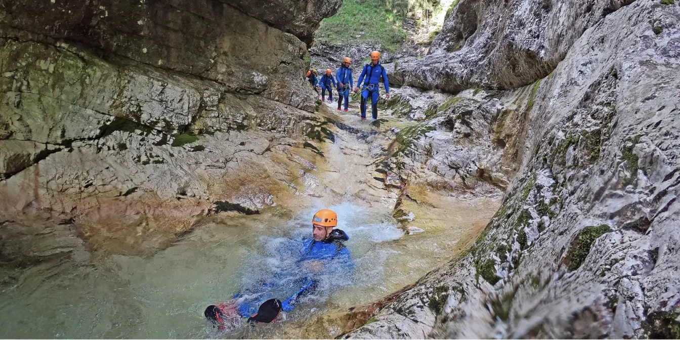 Udeleženec plava skozi kristalni tolmun, skupina se spušča po skali za njim v kanjonu Rio Ronc.