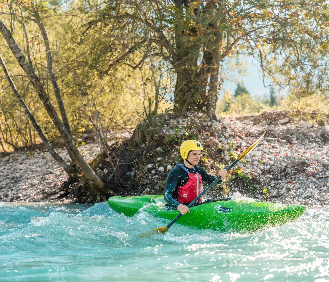 Kajakaš v zelenem kajaku vadi zaveslaje na osončeni Soči.