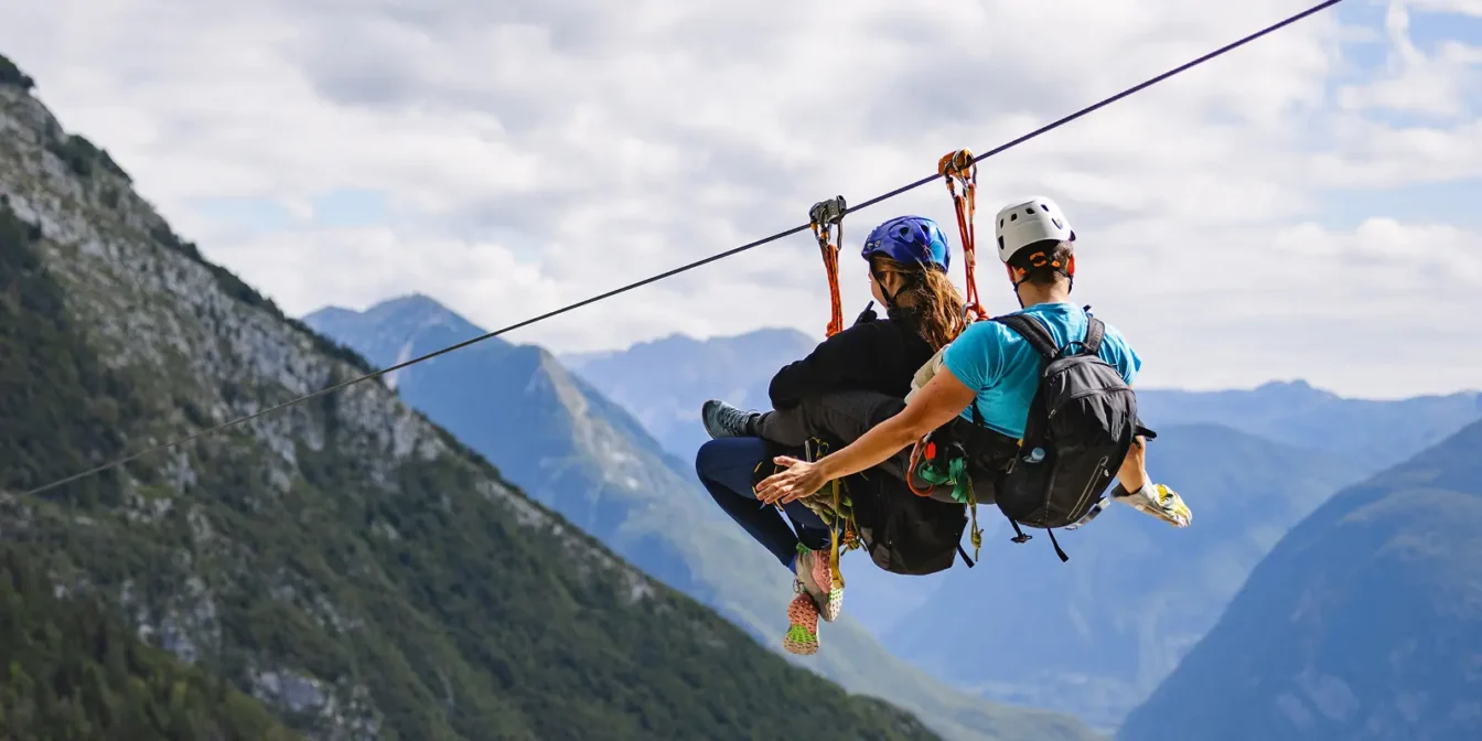 Dva obiskovalca skupaj drsita po jeklenici z razgledom na gorsko dolino.