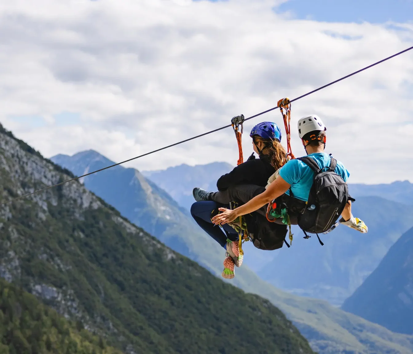 Dva obiskovalca skupaj drvita po jeklenici visoko nad dolino, v ozadju gorski vrhovi nad Bovcem.